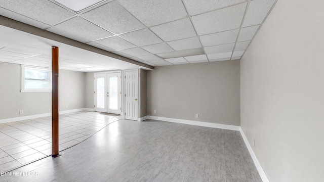 basement with french doors, light tile patterned floors, and a paneled ceiling