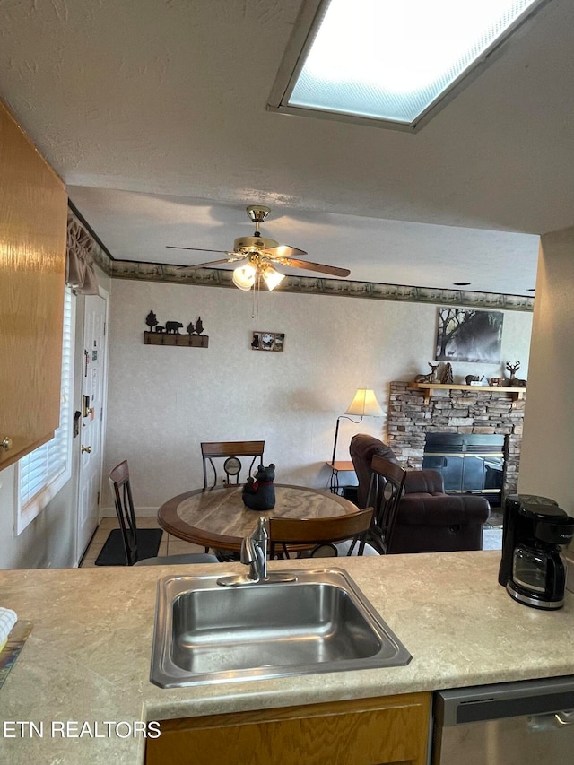 kitchen featuring dishwasher, ceiling fan, sink, and a stone fireplace