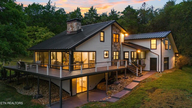 back house at dusk with a sunroom, a yard, and a deck