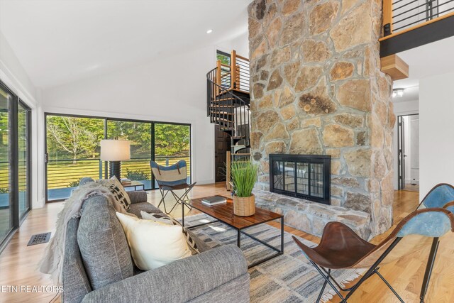 living room with a stone fireplace, light hardwood / wood-style floors, and high vaulted ceiling