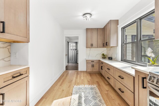 kitchen featuring light brown cabinetry, decorative backsplash, stainless steel electric range, and light wood-type flooring