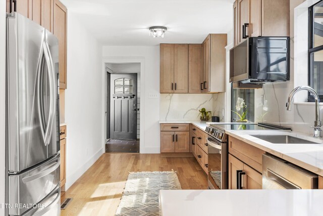 kitchen with stainless steel appliances, sink, light wood-type flooring, and decorative backsplash