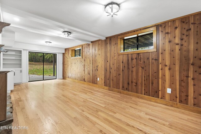 spare room featuring wooden walls, built in features, and light hardwood / wood-style floors