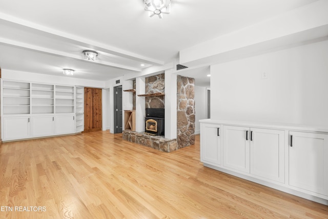 unfurnished living room with built in shelves, light hardwood / wood-style flooring, and a wood stove