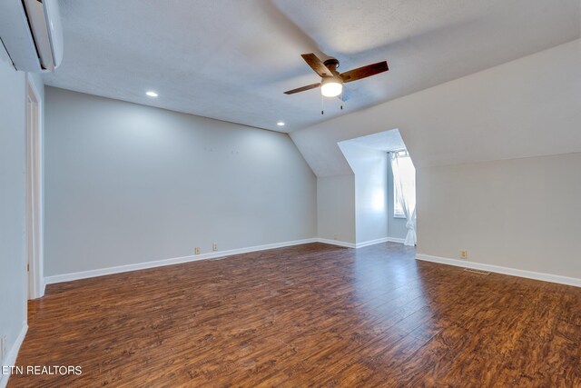 additional living space featuring a textured ceiling, dark hardwood / wood-style flooring, lofted ceiling, ceiling fan, and a wall unit AC