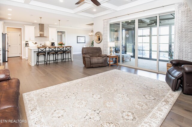 living room with coffered ceiling, beamed ceiling, light hardwood / wood-style floors, crown molding, and ceiling fan