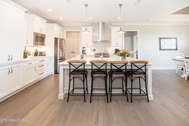 kitchen featuring pendant lighting, appliances with stainless steel finishes, a breakfast bar area, and wall chimney range hood