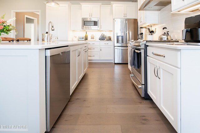 kitchen featuring a center island with sink, hardwood / wood-style floors, appliances with stainless steel finishes, premium range hood, and white cabinets