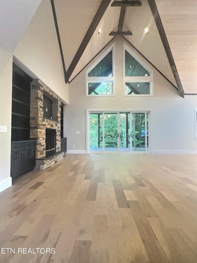 unfurnished living room with high vaulted ceiling, baseboards, beam ceiling, light wood-style flooring, and a stone fireplace