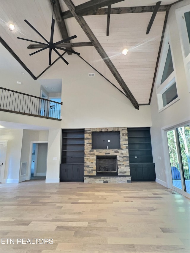 unfurnished living room with light hardwood / wood-style flooring, a stone fireplace, a high ceiling, ceiling fan, and beam ceiling