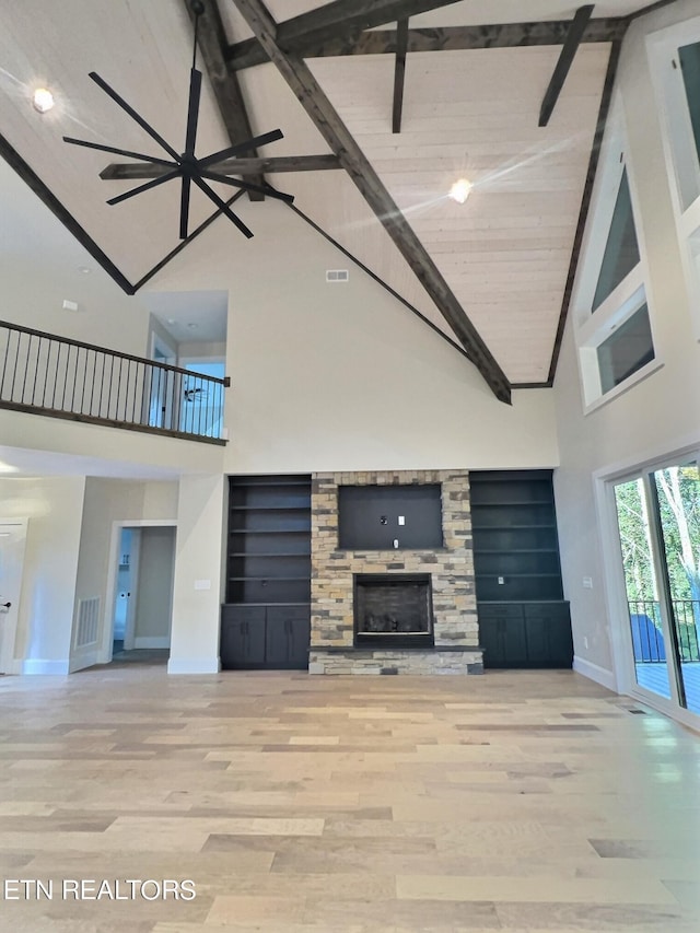unfurnished living room with baseboards, visible vents, wood finished floors, and a stone fireplace