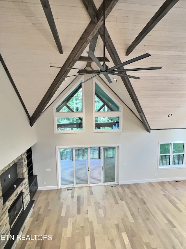 unfurnished living room with high vaulted ceiling, wood finished floors, a stone fireplace, baseboards, and beamed ceiling