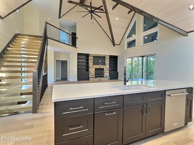 kitchen featuring light countertops, a sink, a fireplace, stainless steel dishwasher, and open floor plan