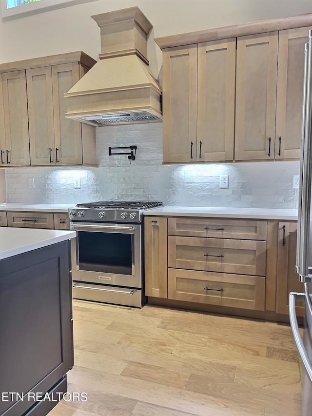 kitchen with light countertops, stainless steel appliances, backsplash, light wood finished floors, and custom exhaust hood
