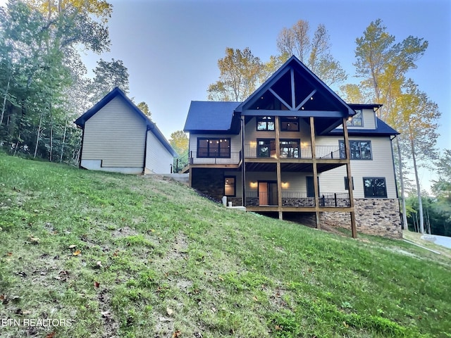rear view of property featuring stone siding, a balcony, and a lawn