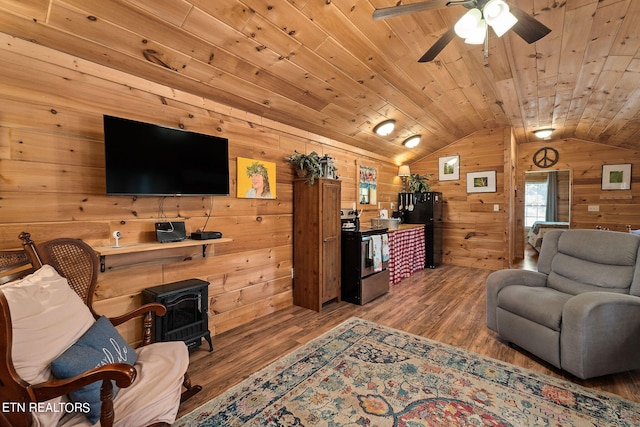 living room featuring a wood stove, wood-type flooring, lofted ceiling, ceiling fan, and wooden walls