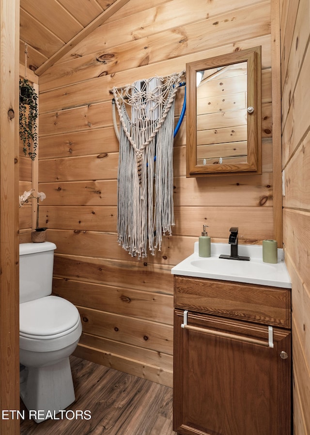 bathroom with vanity, toilet, hardwood / wood-style flooring, lofted ceiling, and wooden walls