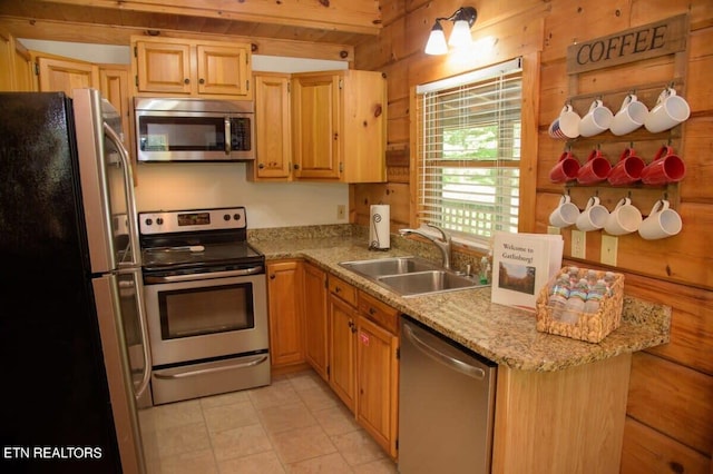 kitchen with appliances with stainless steel finishes, light stone counters, sink, and wooden walls