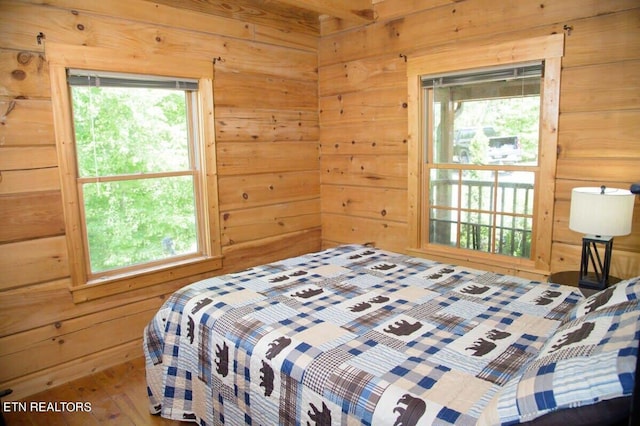 bedroom featuring multiple windows, wood-type flooring, and wooden walls