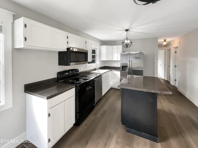 kitchen with dark wood finished floors, a kitchen island, appliances with stainless steel finishes, white cabinetry, and a sink