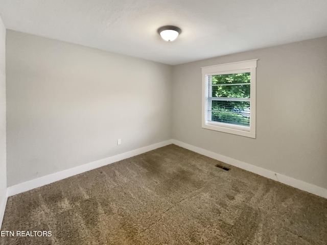 unfurnished room with dark colored carpet, visible vents, and baseboards