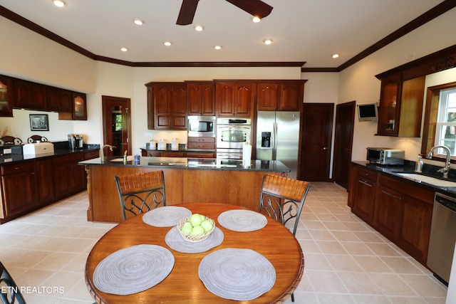 kitchen with light tile patterned floors, stainless steel appliances, sink, ceiling fan, and a center island with sink