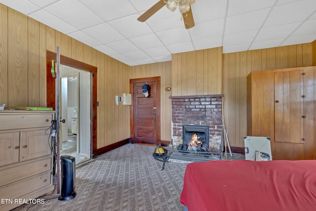 bedroom with carpet floors, a brick fireplace, wooden walls, and a drop ceiling