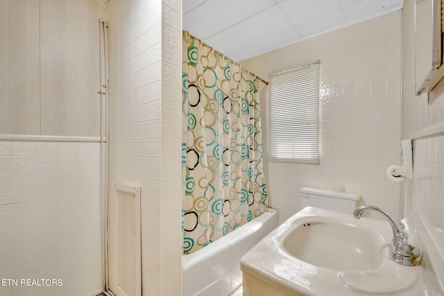 full bathroom with shower / bath combination with curtain, a sink, toilet, and tile walls