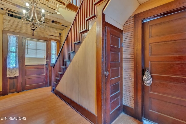 entryway featuring stairway, a notable chandelier, light wood-style flooring, and wooden walls