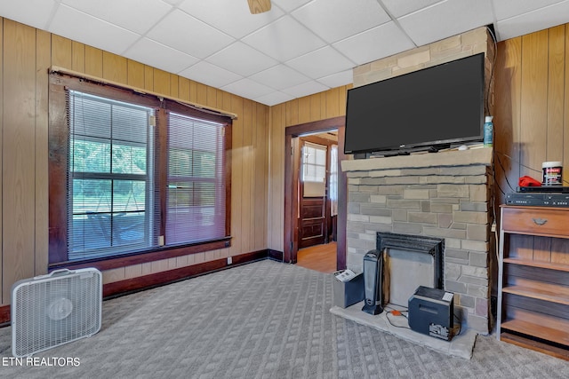 living area featuring a fireplace, carpet flooring, wood walls, a drop ceiling, and baseboards