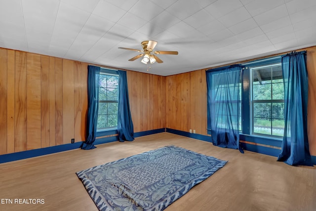 interior space with wood walls, wood finished floors, a ceiling fan, and baseboards