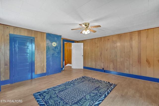 interior space with ceiling fan, wood walls, wood finished floors, and baseboards