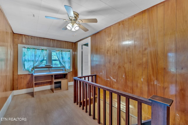 hallway with wood walls, baseboards, wood finished floors, and an upstairs landing