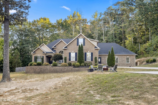 traditional-style home featuring a front lawn, a fire pit, brick siding, and roof with shingles