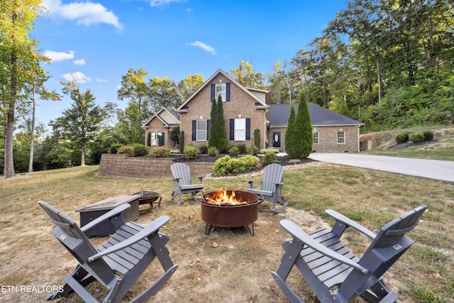 rear view of property featuring brick siding, a fire pit, and a lawn