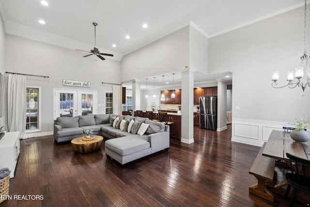living room featuring crown molding, a towering ceiling, decorative columns, dark wood finished floors, and ceiling fan with notable chandelier