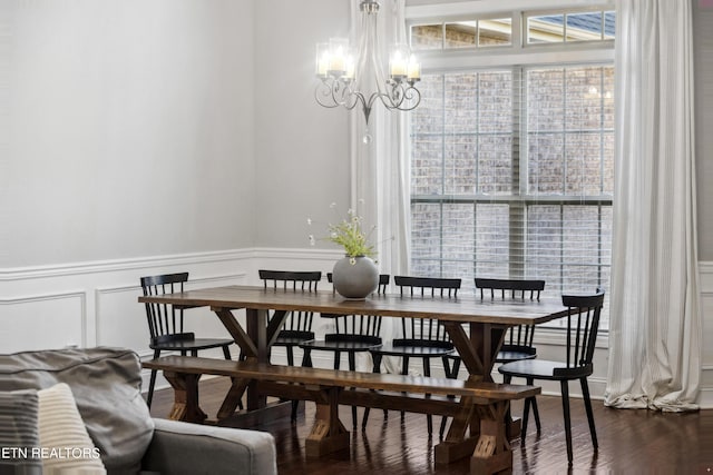 dining space featuring a decorative wall, a wainscoted wall, dark wood-type flooring, and a chandelier