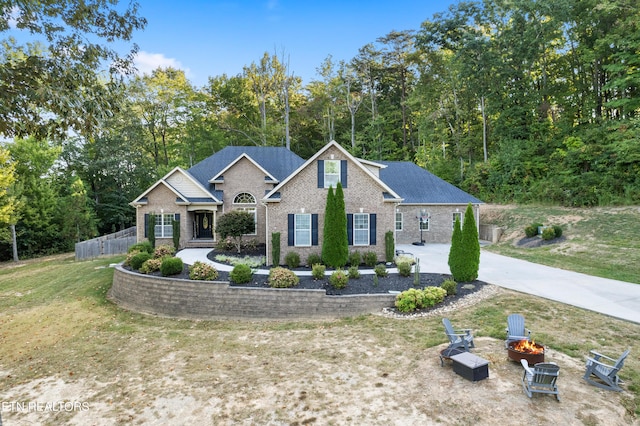view of front of home with fence, driveway, a front yard, brick siding, and a fire pit