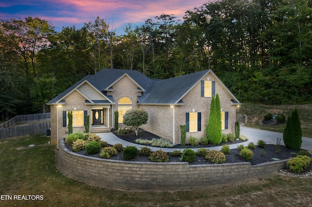 view of front of property featuring a yard, brick siding, concrete driveway, and fence