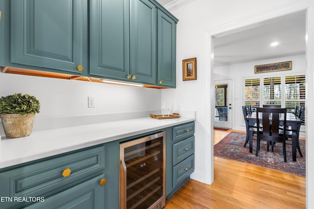 bar featuring wine cooler, blue cabinets, ornamental molding, and light wood-type flooring