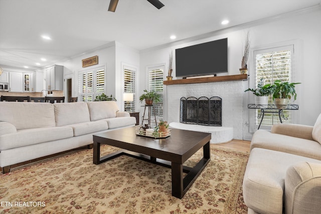 living room featuring a fireplace, light hardwood / wood-style floors, ceiling fan, and crown molding