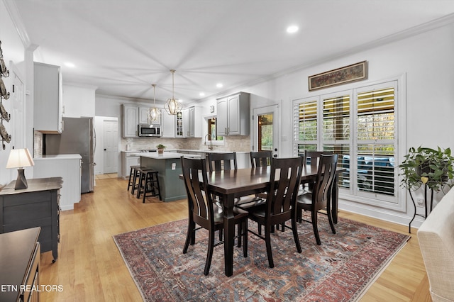 dining area with sink, light wood-type flooring, crown molding, and a chandelier