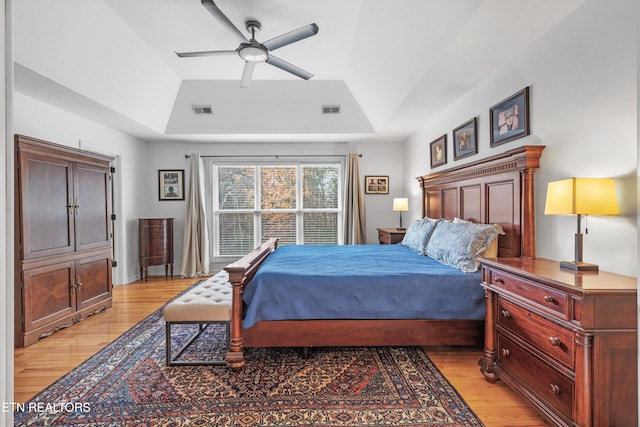 bedroom with ceiling fan, light hardwood / wood-style floors, vaulted ceiling, and a tray ceiling