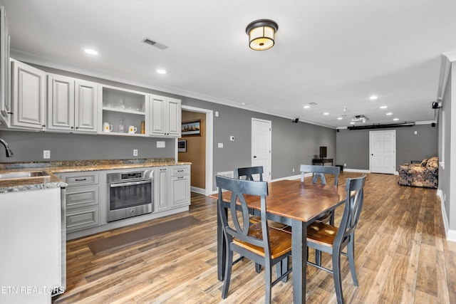 dining space featuring a barn door, sink, light wood-type flooring, and crown molding