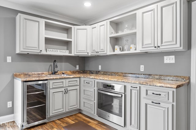 kitchen with sink, dark wood-type flooring, beverage cooler, light stone counters, and oven