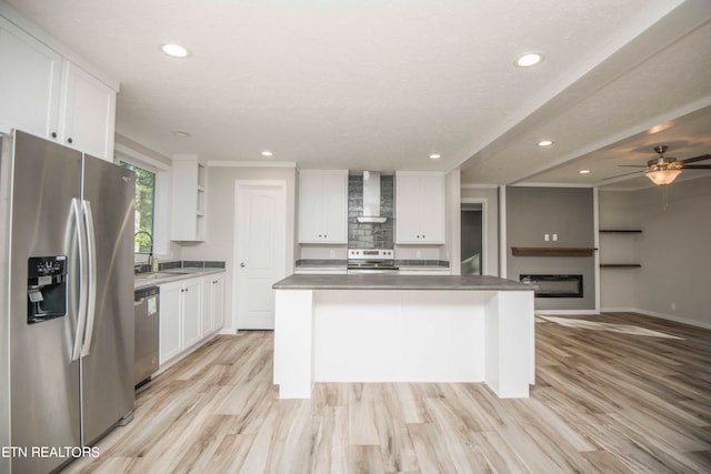 kitchen featuring white cabinets, stainless steel appliances, a kitchen island, and wall chimney exhaust hood