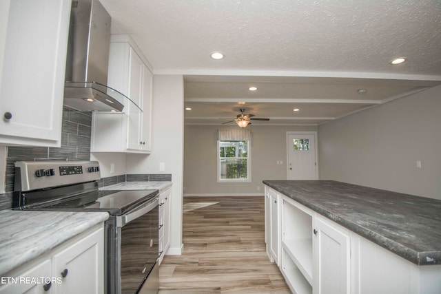 kitchen featuring stainless steel electric stove, wall chimney range hood, white cabinetry, beamed ceiling, and ceiling fan