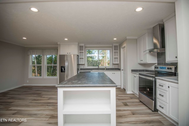 kitchen featuring appliances with stainless steel finishes, white cabinets, light wood-type flooring, a center island, and wall chimney range hood