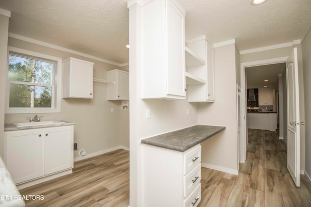 kitchen with sink, light wood-type flooring, white cabinetry, and a textured ceiling