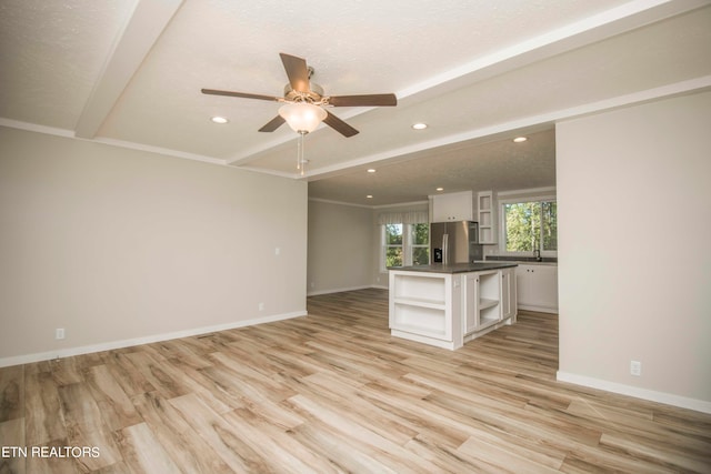 unfurnished living room with light wood-type flooring, a textured ceiling, beam ceiling, and ceiling fan